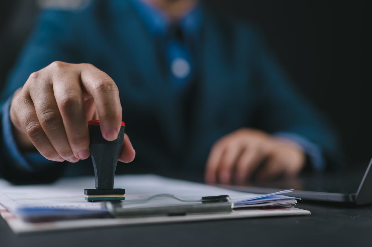 Close-up of a notary's hand stamping an approved document at a desk